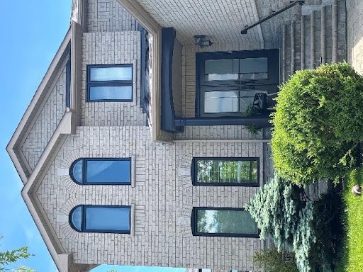 Exterior view of a light brick home featuring multiple black-framed energy-efficient windows and custom arch accent windows.