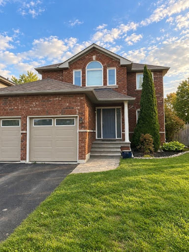 Exterior front view of a two-story red brick home with tan garage doors, a blue front entry door, and a green front lawn.