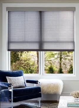 Living room interior view of double-hung white windows equipped with a pull-down cellular energy-efficient window shade next to a navy blue armchair.